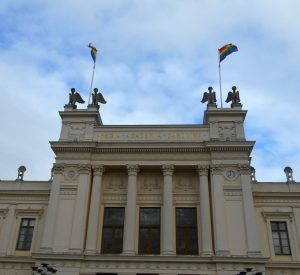 Photo of the main university building with two rainbow flags hoisted from it